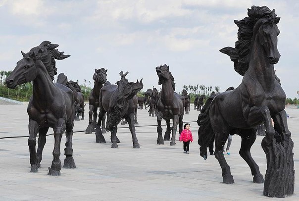 Девочка гуляет среди статуй бронзовых лошадей, символизир