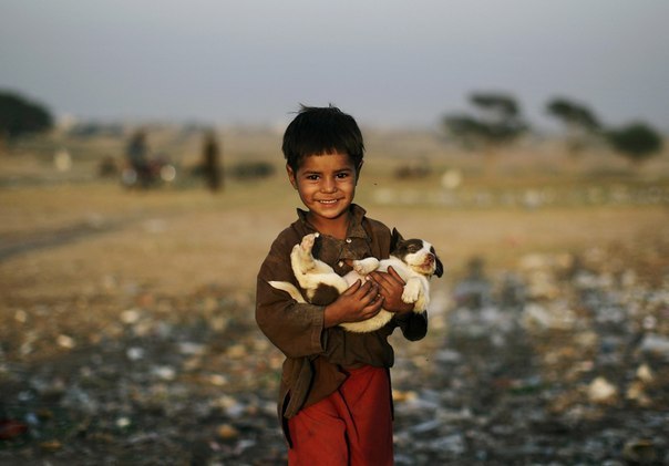 Пятилетний мальчик, беженец из Афганистана, несёт щенка, найденного на свалке на окраине Исламабада, Пакист