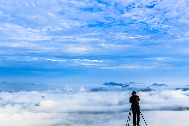 Мужчина фотографирует облака над городом с горы Yangbaeksan, Юж